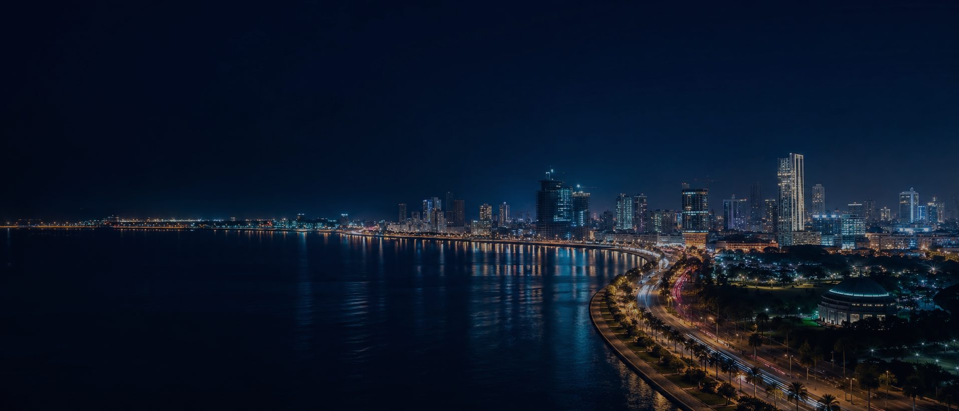 Marginal de Luanda à noite, com a orla iluminada e o skyline da cidade.